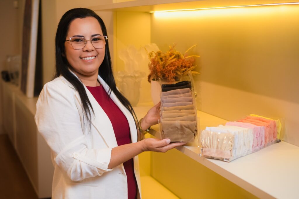 Sulamyta segura um organizador transparente com peças dobradas, ao lado de uma prateleira com outros organizadores da loja